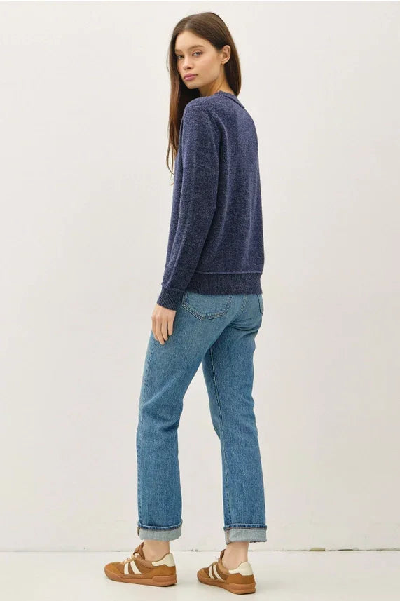 Woman wearing navy blue crew neck pullover with exposed seams, light blue cuffed jeans and brown sneakers