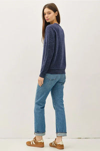Woman wearing navy blue crew neck pullover with exposed seams, light blue cuffed jeans and brown sneakers