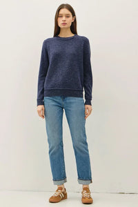 Woman wearing navy blue crew neck pullover with exposed seams, light wash cuffed jeans and brown sneakers