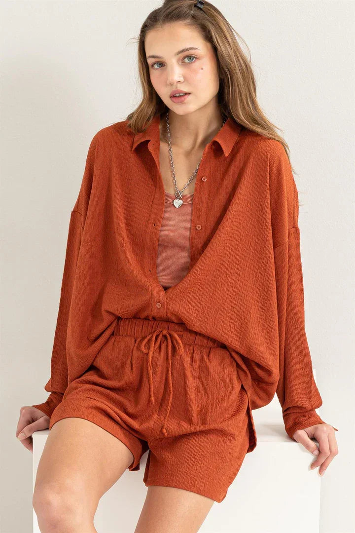 Woman wearing a flowy crinkle knit shirt and shorts set in vibrant orange