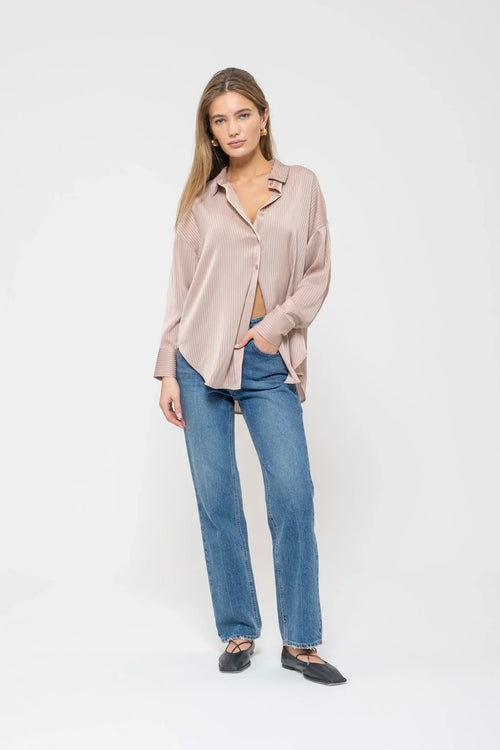 Woman in a satin pinstripe button-up top with blue jeans, showcasing stylish casual wear