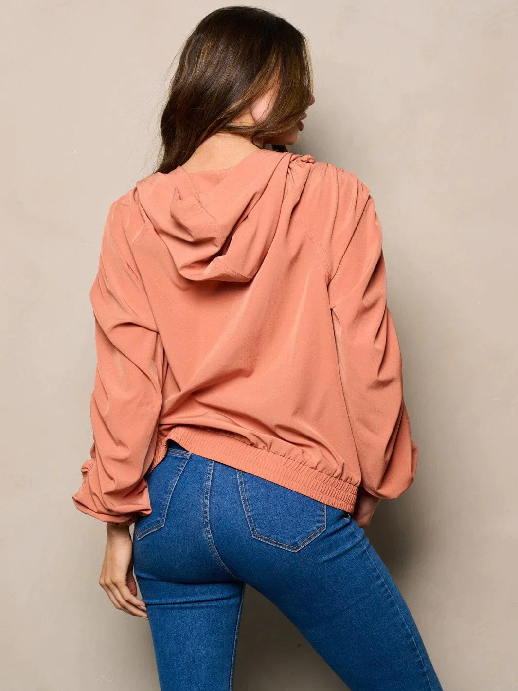 Woman in peach sweatshirt with long ruched sleeves and pockets, showcasing hooded jacket