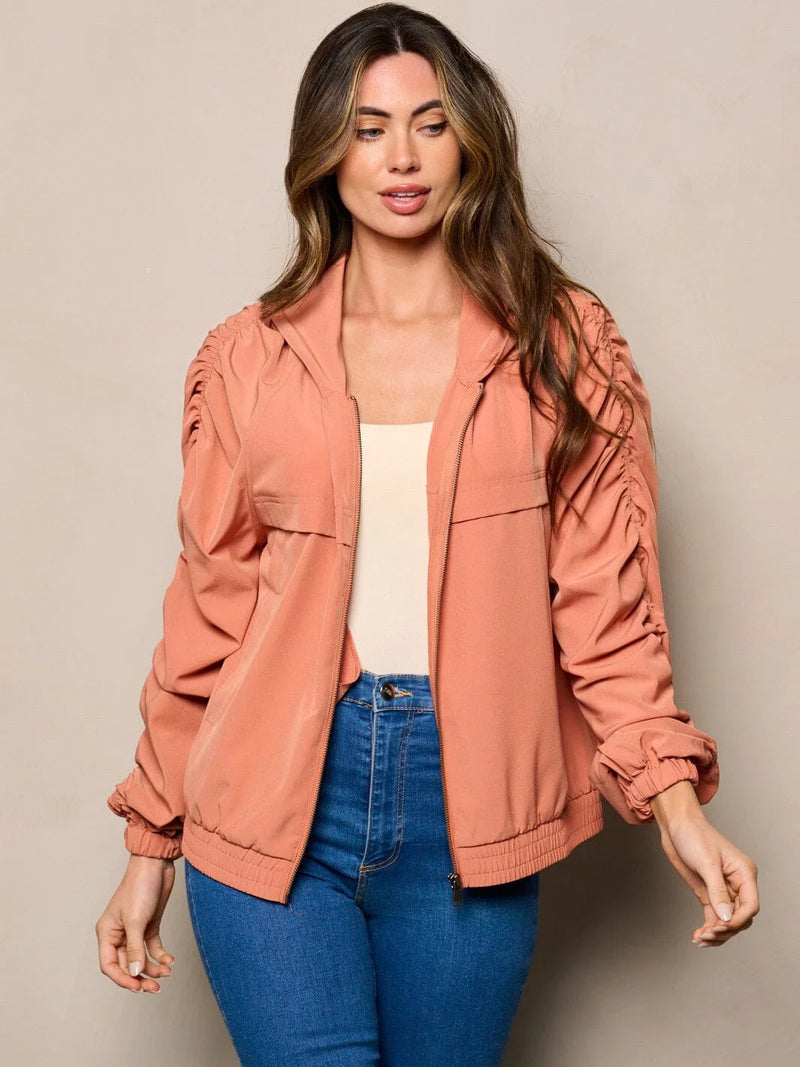 Woman in a pink jacket with long ruched sleeves and pockets, posing stylishly