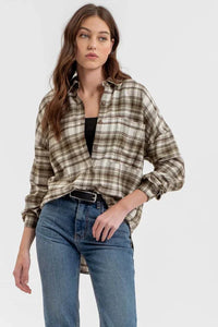 Woman in a long sleeve button down plaid shirt over a black top and blue jeans