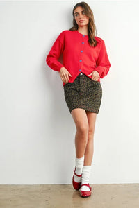 Woman modeling leopard print mini skirt with red cardigan and Mary Jane shoes showcasing women’s boho chic clothing