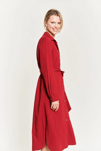 Woman in a red trench coat wearing a solid button belted long dress