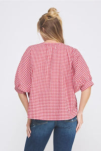 Woman wearing a red and white gingham dolman sleeve blouse with distressed blue jeans