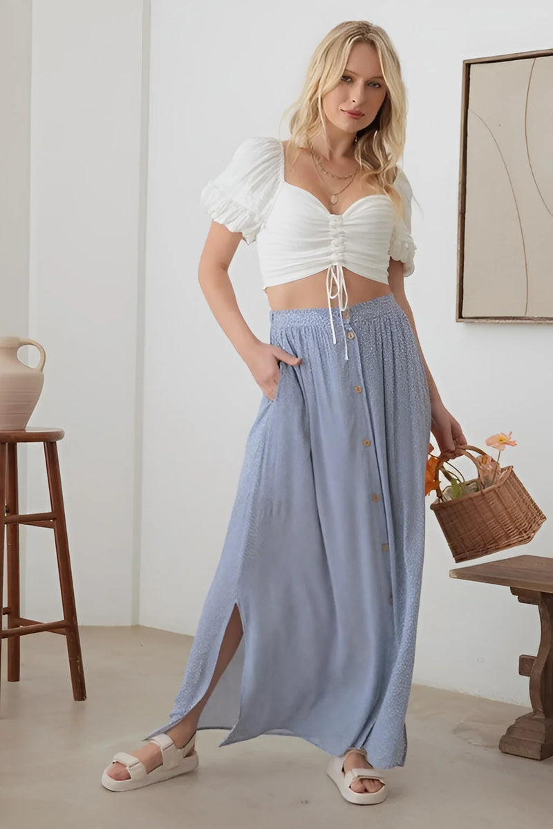 Woman in a room with a basket, showcasing the BOHO Front Button Floral Maxi Skirt