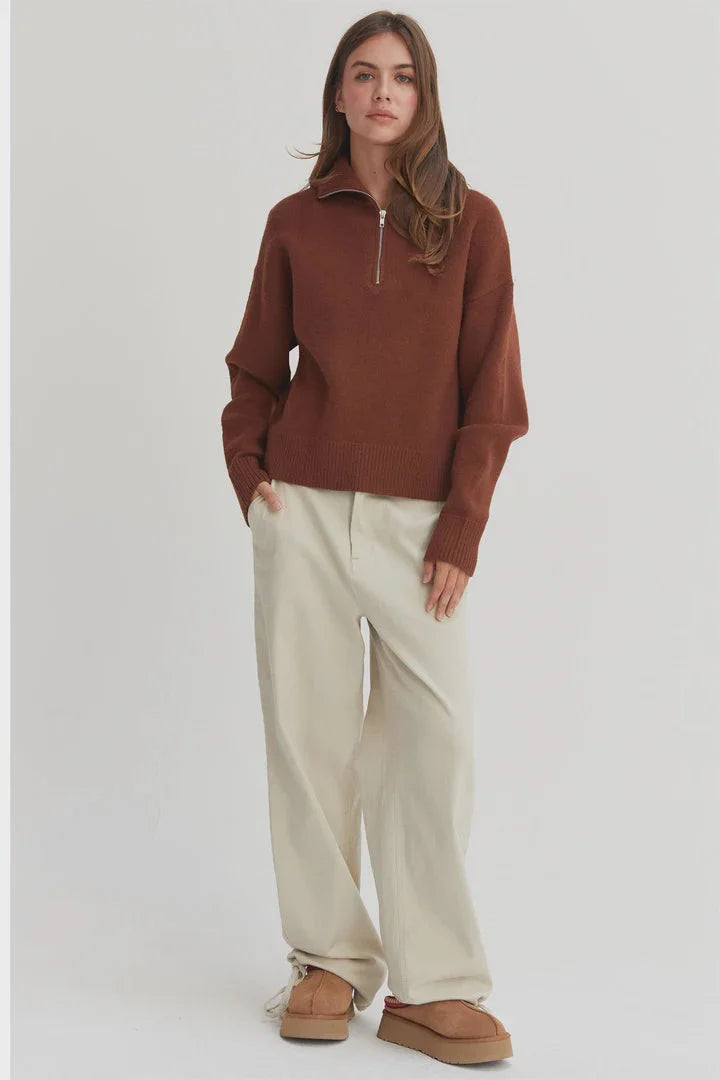 Woman in a rust-colored drop shoulder half zip sweater and cream-colored pants