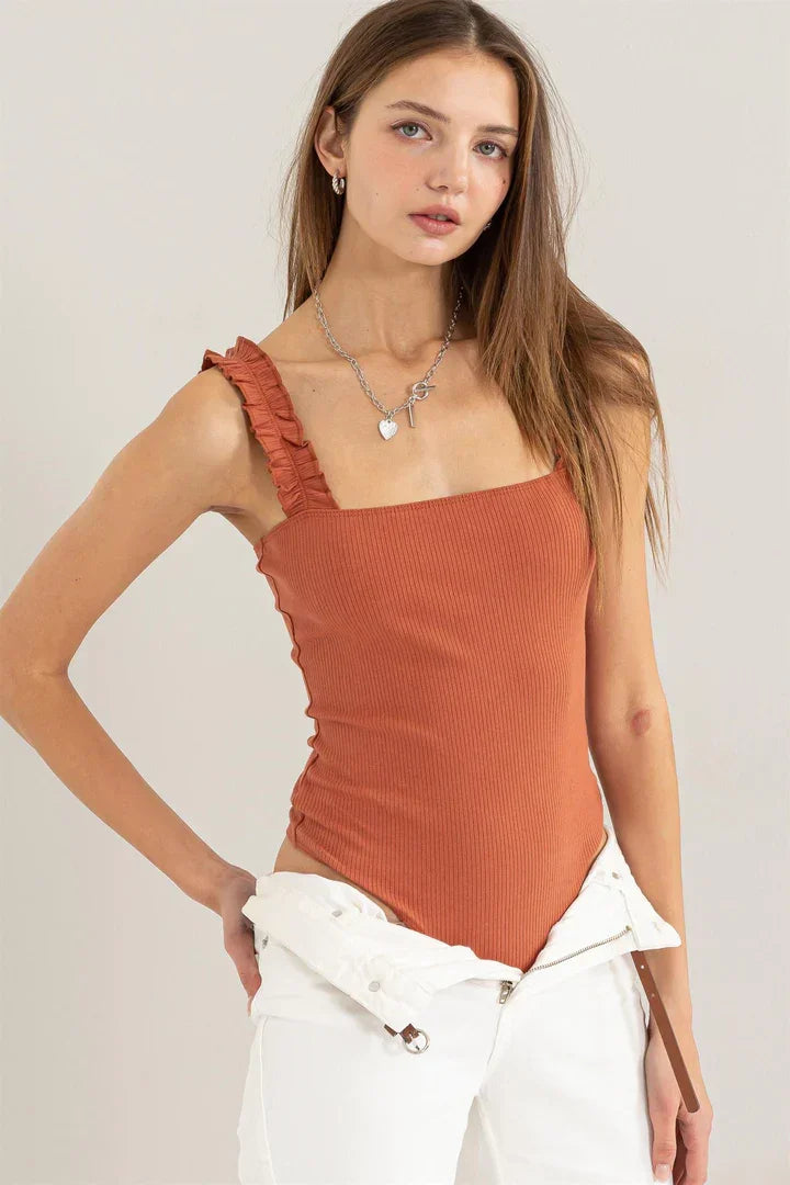 Woman wearing a rust top featuring a ribbed ruffle strap bodysuit design