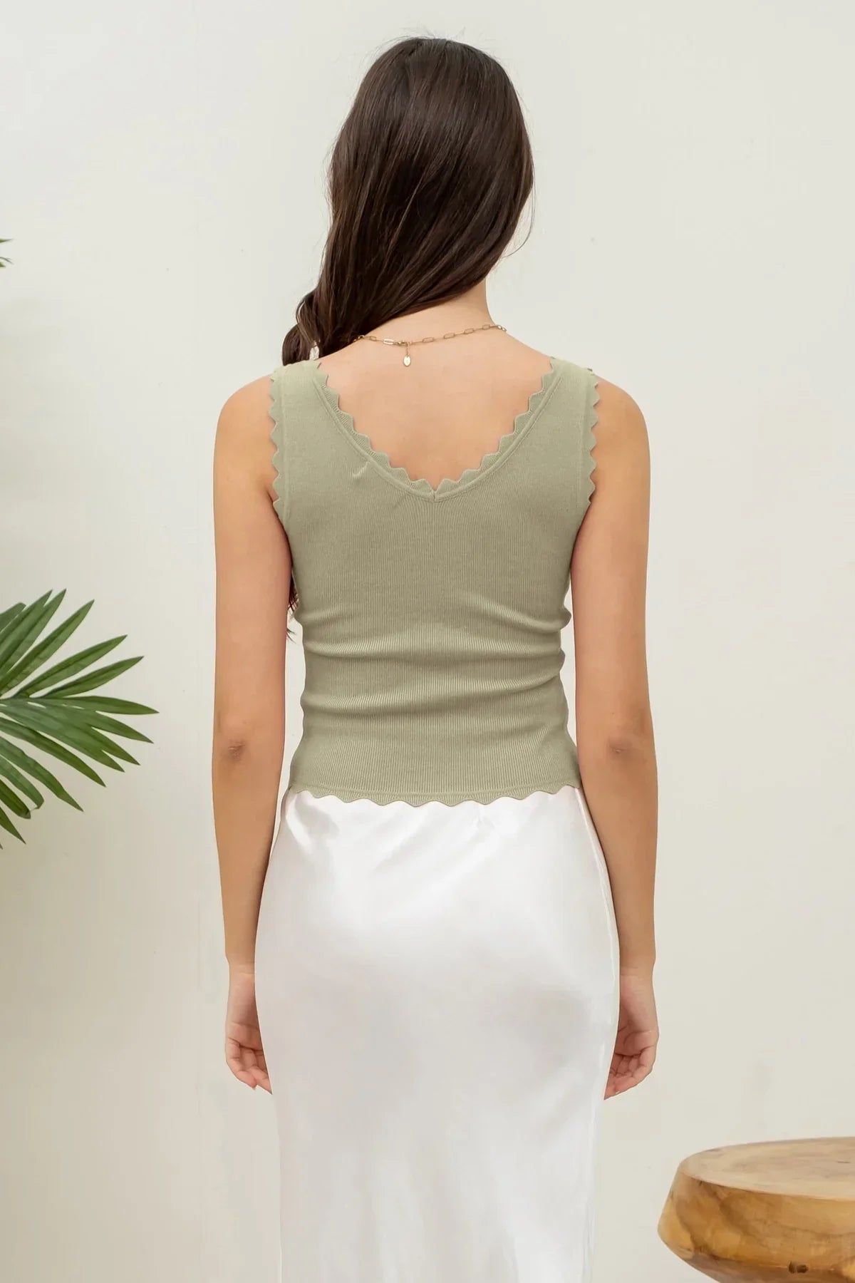 Woman in sage green scallop edge sleeveless top and white skirt, viewed from behind