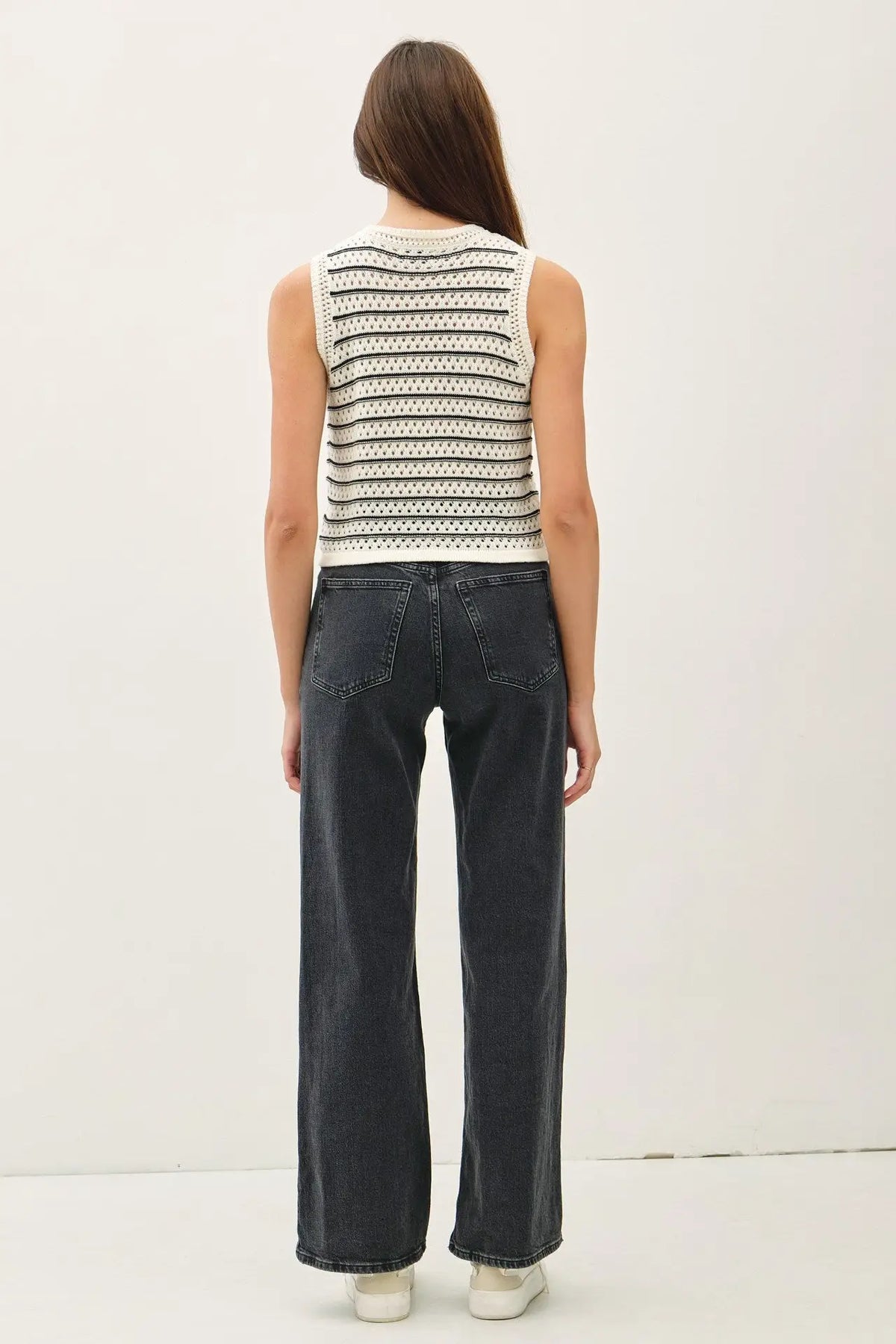 Woman wearing a chunky knit striped sweater tank paired with wide-leg jeans