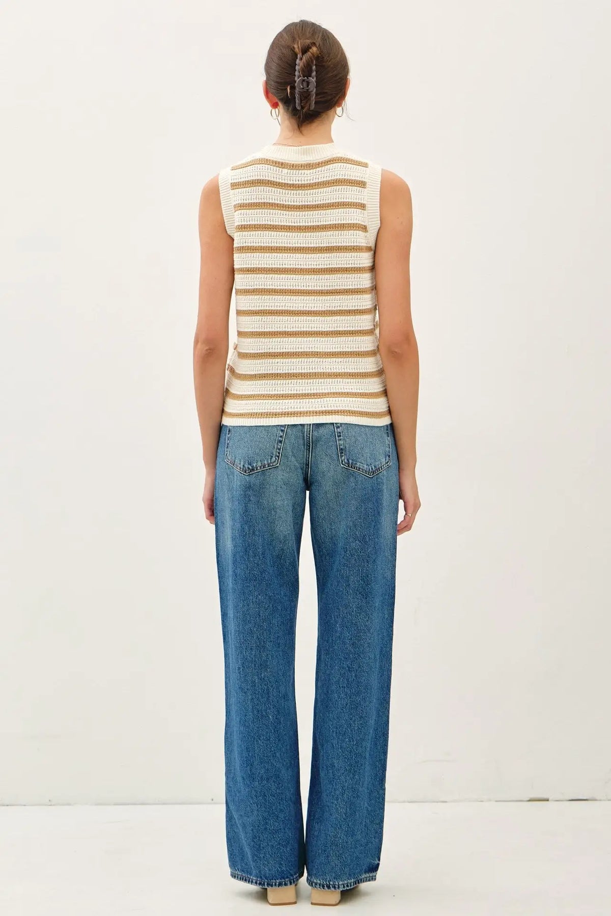 Woman wearing a chunky knit striped sweater tank with contrast accents and blue jeans