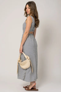 Woman in a sleeveless stripe side slit maxi dress with a beige handbag