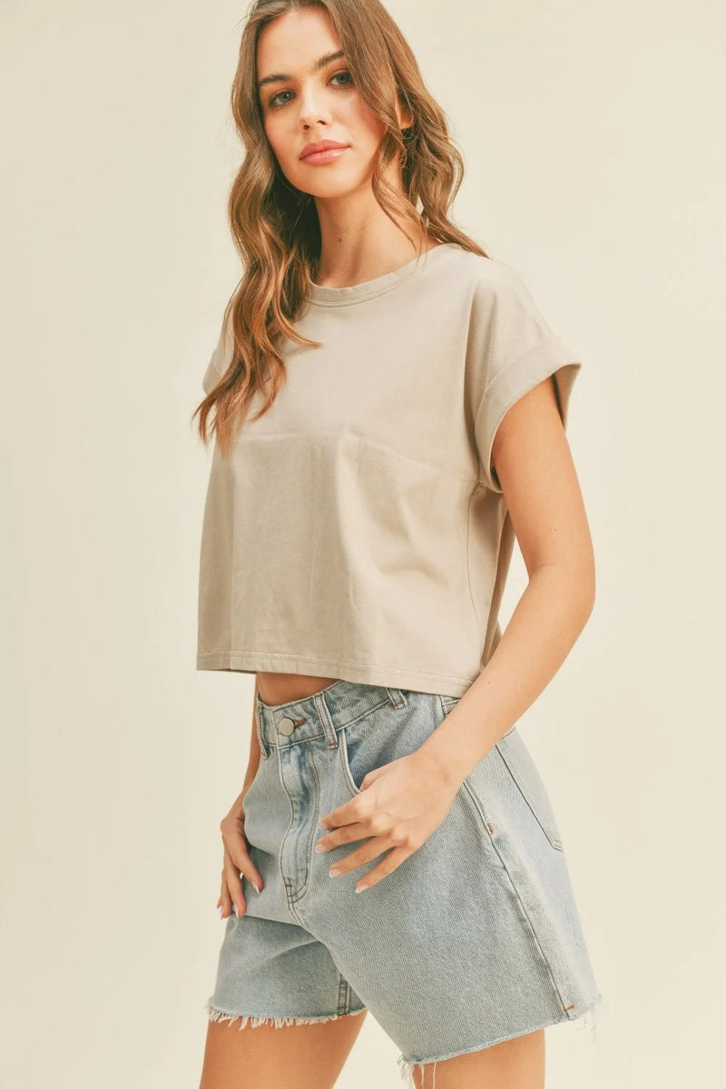 Woman wearing a tan round neck cuffed sleeve top with light wash denim shorts