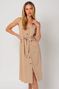 Woman in tan sleeveless button dress with band tie detail and pockets at midi length