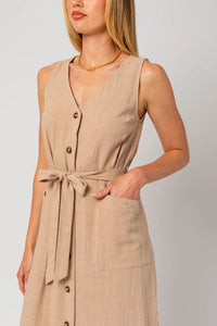 Woman in tan linen sleeveless button midi length dress with band tie and pockets