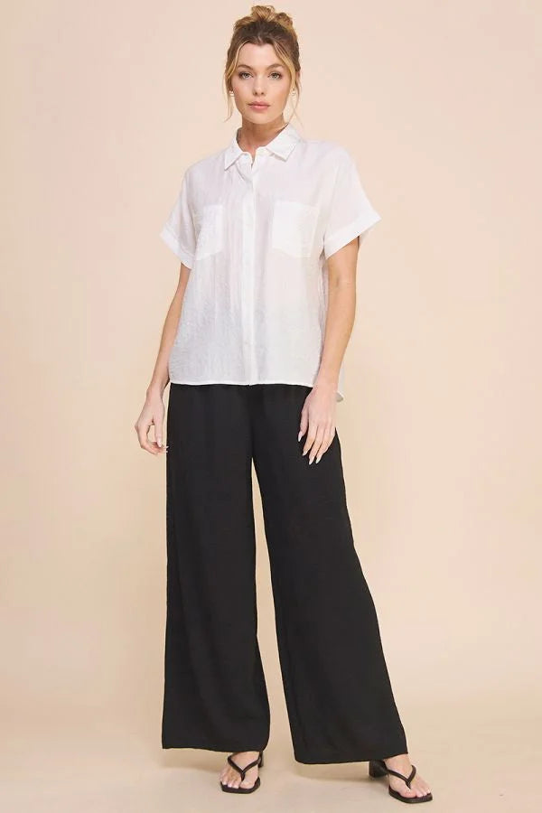 Woman in a white collared textured short sleeve button front shirt and black wide-leg pants