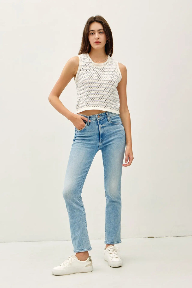 Woman wearing a white chunky knit sweater tank with light blue jeans, stylish striped sweater tank