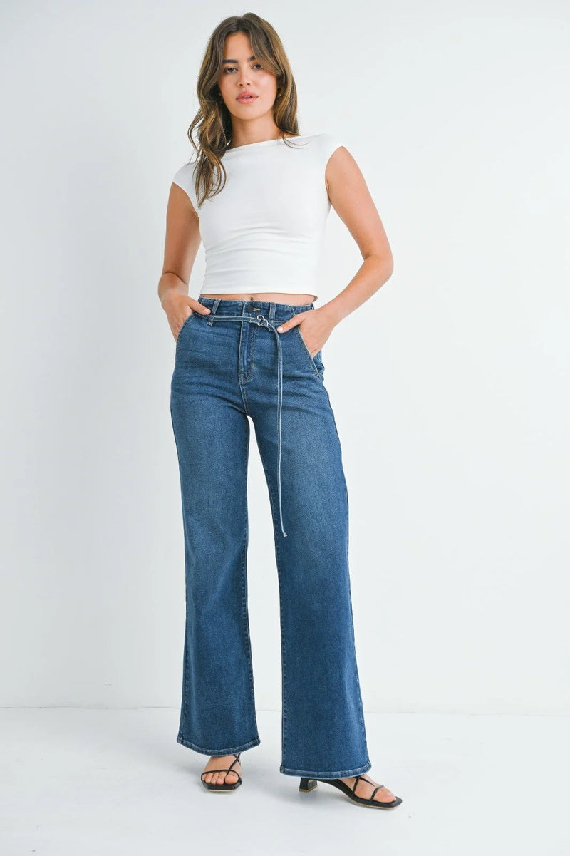 Woman in white crop top and blue jeans showcasing dark denim belted wide leg style