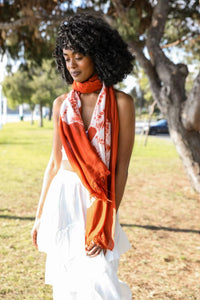 Woman in a white dress showcasing a tie dye lightweight scarf in vibrant orange