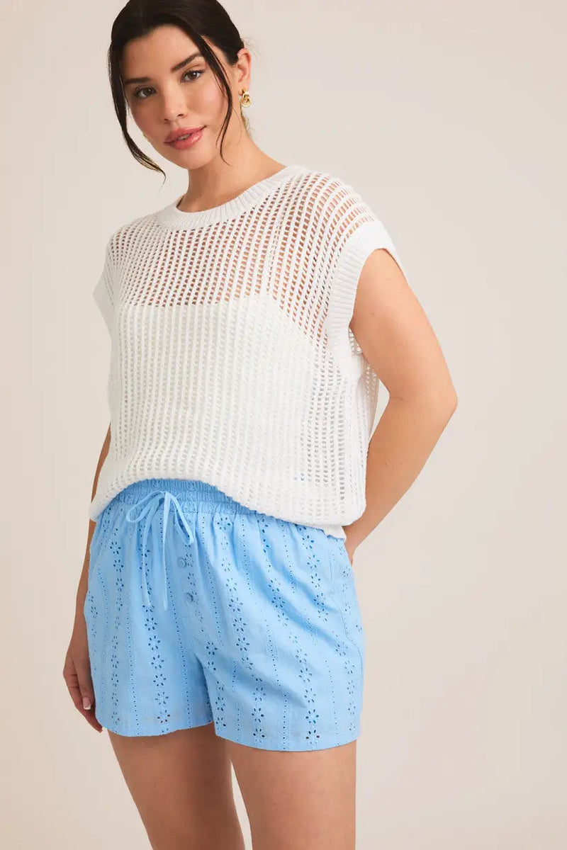 Woman in a white knit top and blue eyelet shorts from Shop Daisy’s oversize sleeveless collection