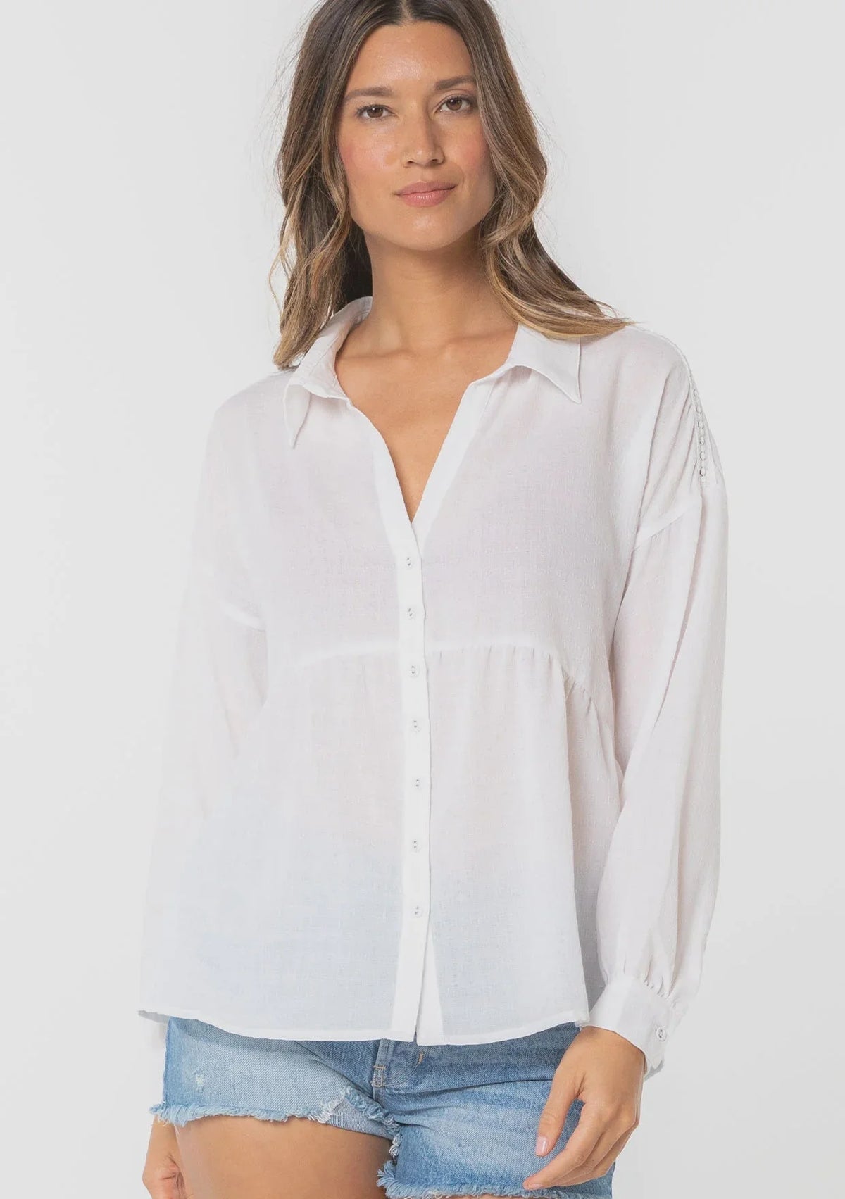 Woman modeling bohemian long sleeve tiered button front top with distressed denim shorts