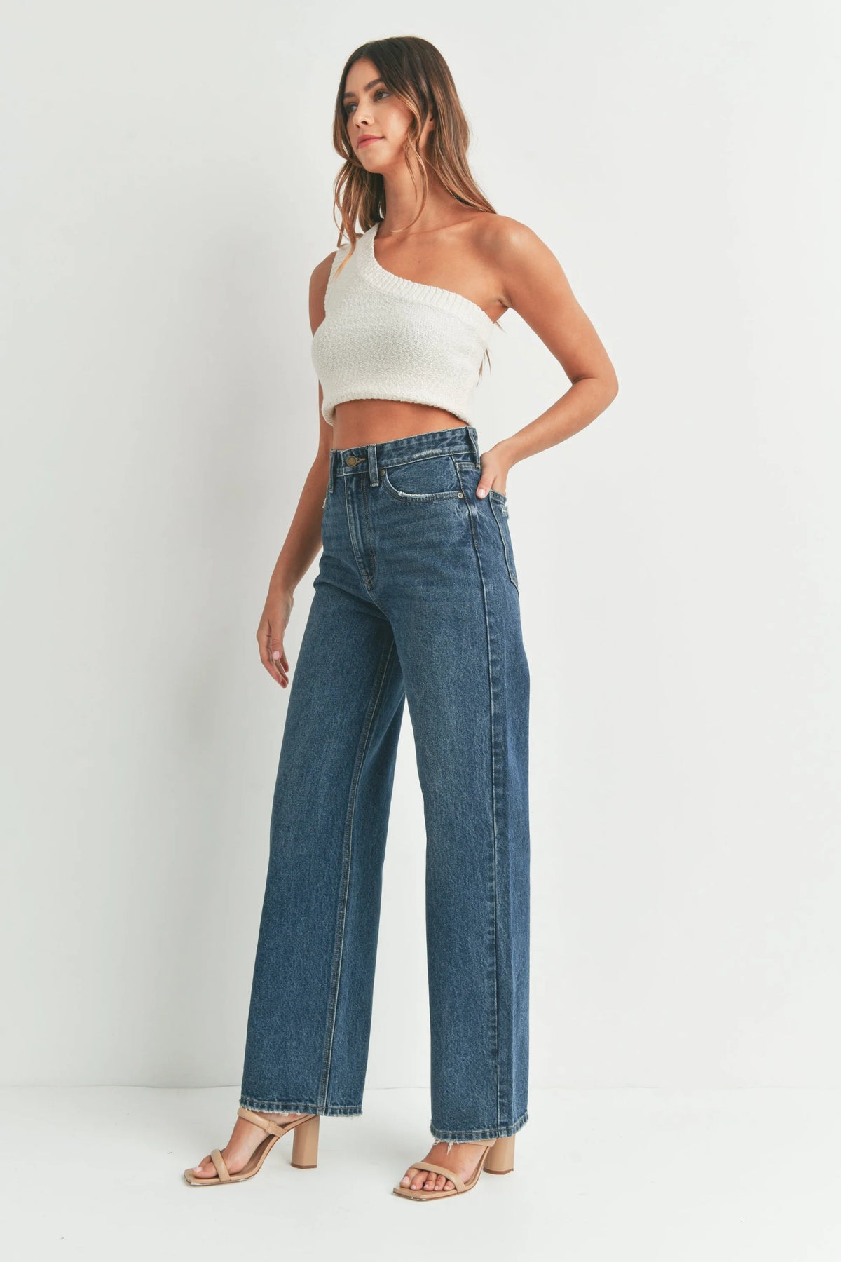 Woman in a white one-shoulder crop top and high waisted skater jeans