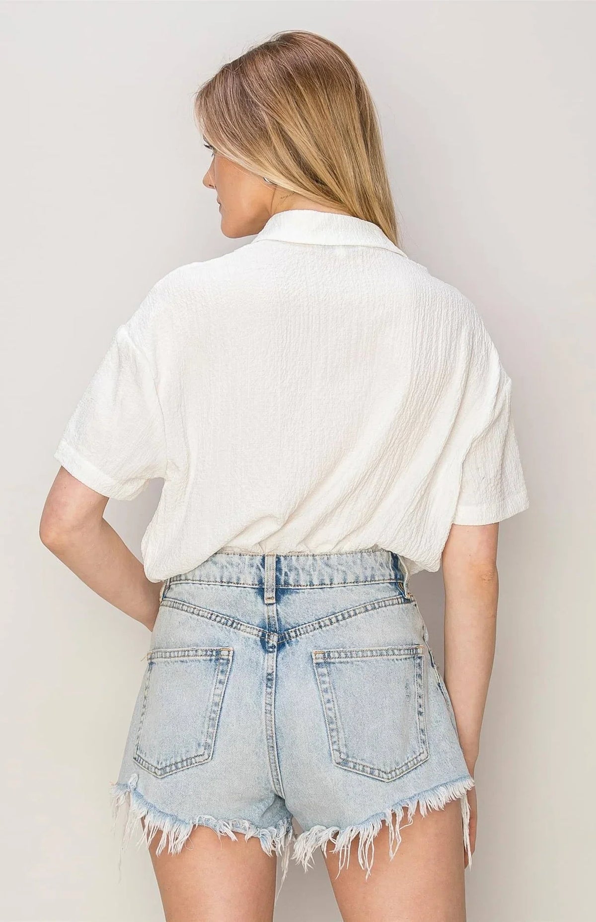 Woman in white oversized button down top and denim shorts, exuding boho free spirit style