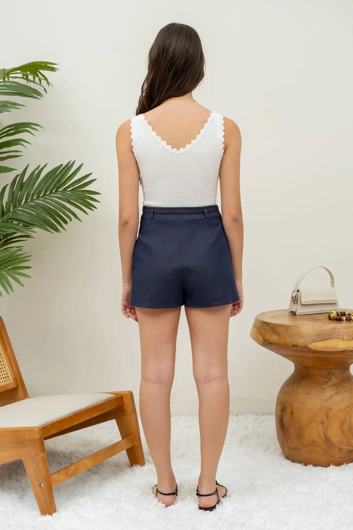 Woman in a scallop edge sleeveless crop top and navy blue shorts, seen from behind