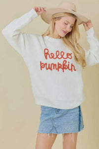 Woman in a white crew neck sweater with hello pumpkin text, denim skirt, and beige hat