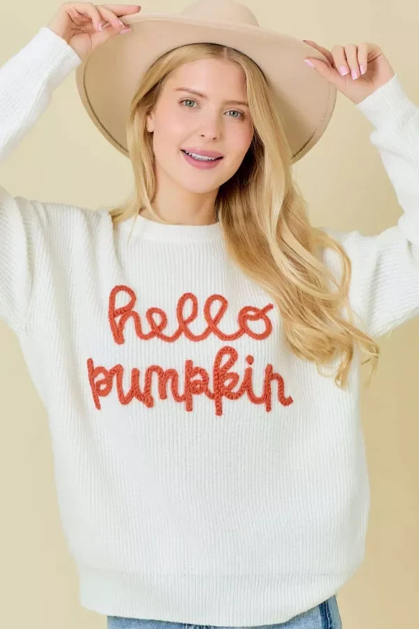 Woman in a white crew neck sweater with hello pumpkin text and a beige hat