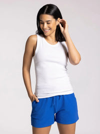 Woman in white EDLIN BASIC TANK and blue shorts, smiling and touching her hair