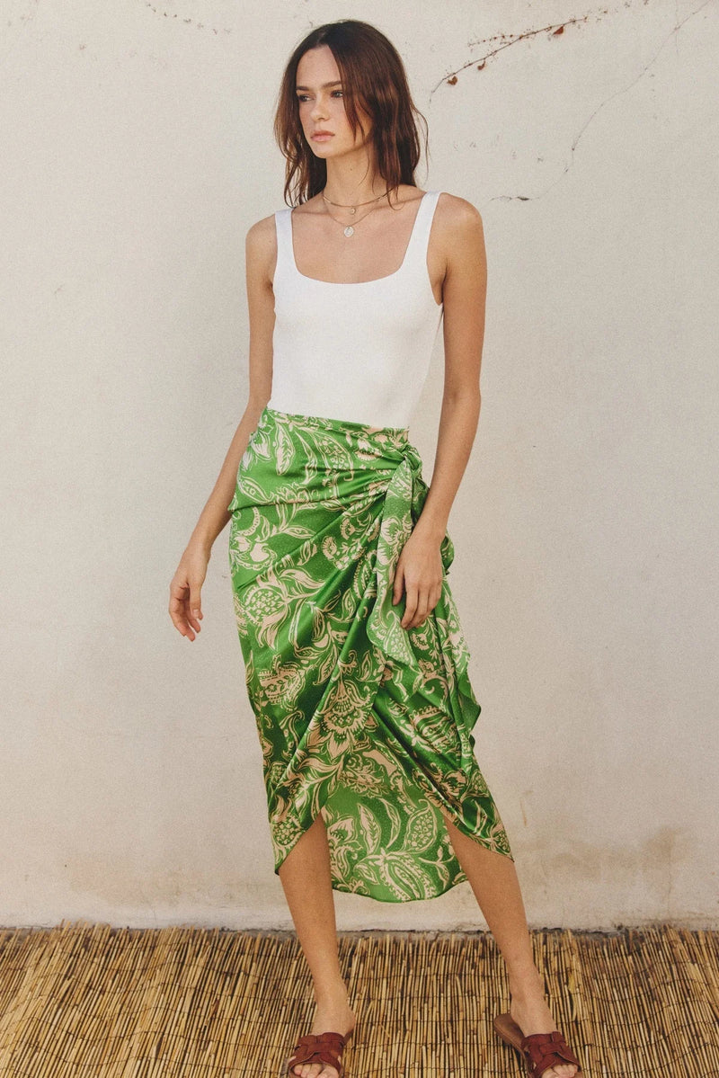 Woman in a white tank top and green tropical wrap skirt embodying a boho, free spirit style