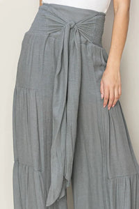 Woman in a white tank top and grey ruched tiered pants showcasing a stylish look