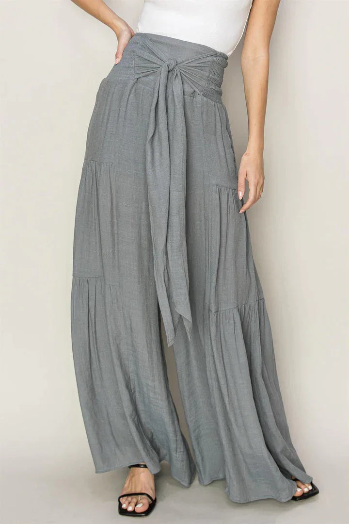 Woman in a white tank top and grey ruched tiered pants, showcasing stylish fashion