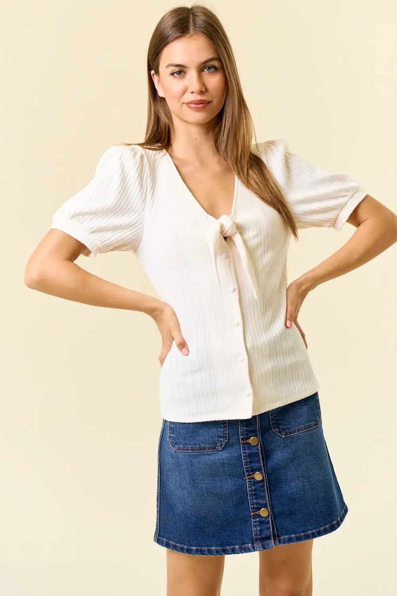 Woman wearing a white tie-front pointelle knit blouse and denim skirt