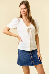 Woman wearing a white pointelle knit blouse with tie-front detail and denim skirt
