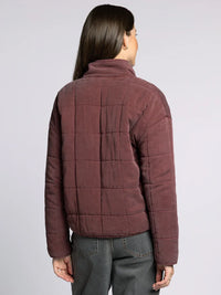 Woman wearing dark plum quilted supply brina jacket with high collar over dark grey pants