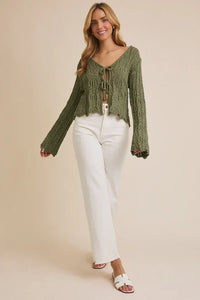 Woman wearing green open knit cardigan with bell sleeves and tie bell front at Fashion Retail Store