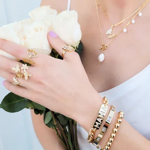 Woman’s hand with gold butterfly rings and bracelets, holding white roses, showcasing the CZ Script Heart Ring