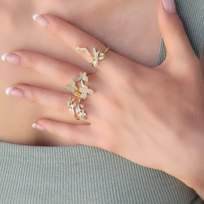 Woman’s hand with tied bow ribbon gold rings featuring butterfly and leaf designs with sparkling stones
