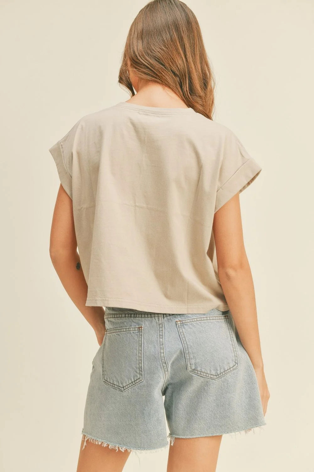 Woman wearing a light beige round neck cuffed sleeve top with light wash denim shorts