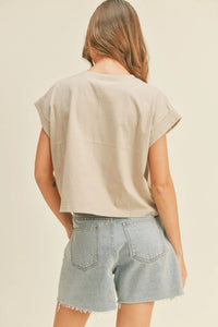 Woman wearing a light beige round neck cuffed sleeve top with light wash denim shorts