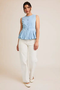 Woman wearing a light blue sleeveless denim top with bubble hem and white pants