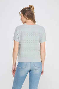 Woman wearing a light green short sleeve patterned fine gauge knit Dolman top with blue jeans