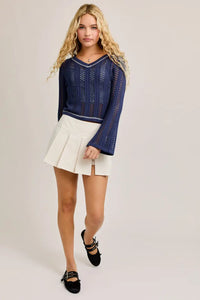 Woman’s navy crochet contrast stitch V-neck long sleeve top paired with white pleated skirt