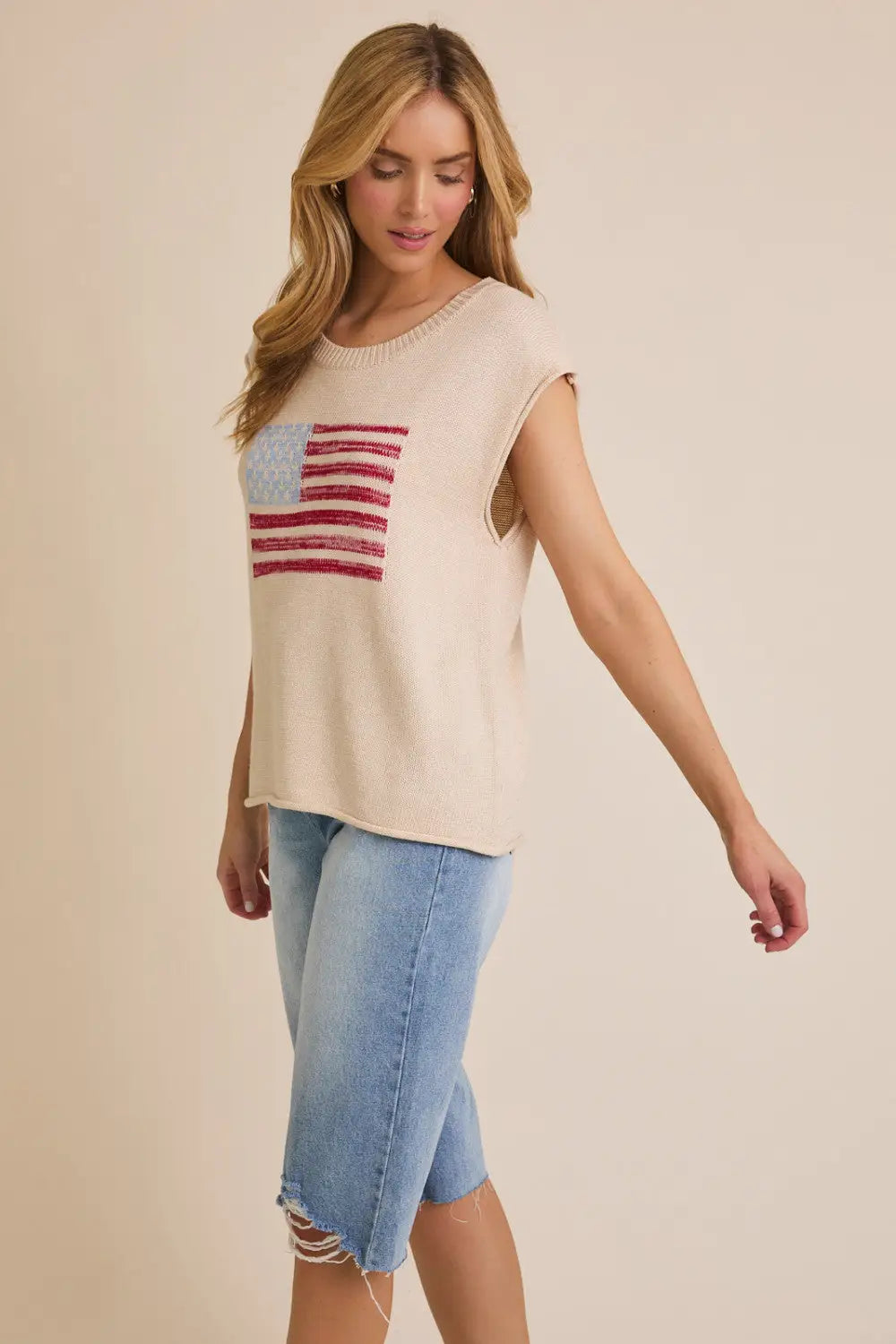 Woman wearing a patriotic sleeveless top with wide shoulder USA flag design and denim shorts