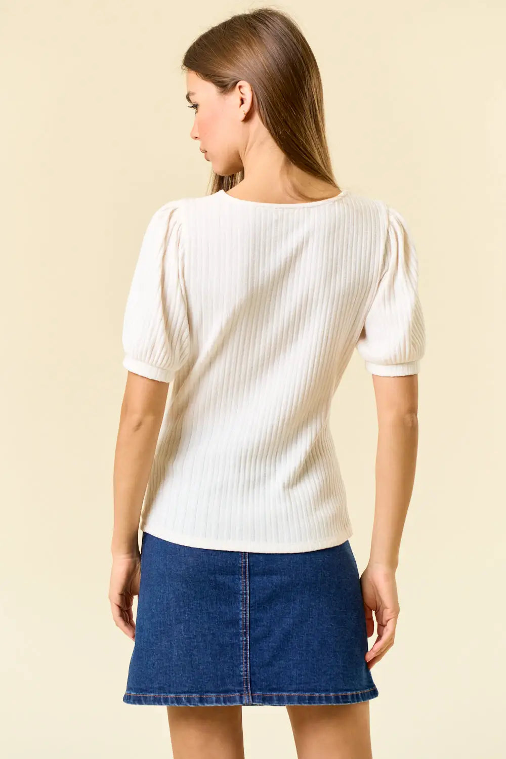 Woman wearing a white pointelle knit blouse with puff sleeves and denim skirt