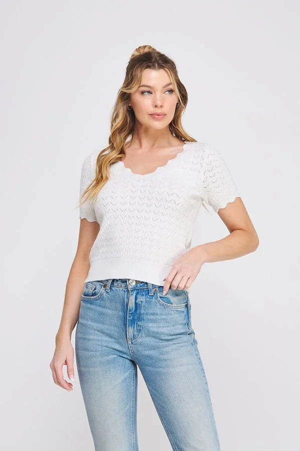 Woman wearing a white pointelle V-neck knit top with scallop edges and blue jeans